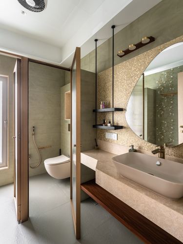 Bathroom vanity with round mirror, gold penny-tile wall, stone counter and vessel sink beside toilet alcove