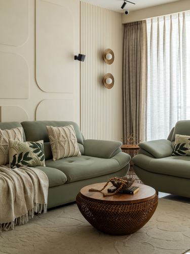 Sage green sofas around a round rattan coffee table against a paneled beige wall with sconces