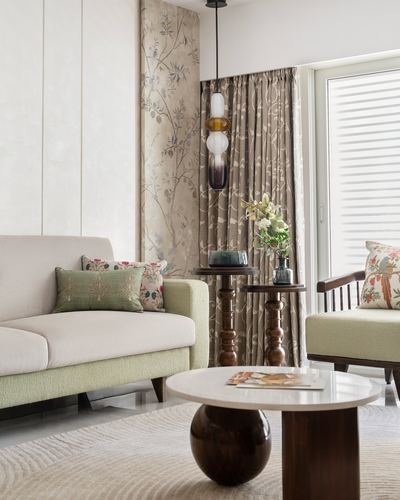 Living room corner with cream sofa, floral wallpaper, turned wood side tables and round marble coffee table