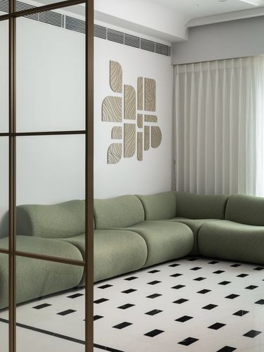 Sage green sectional sofa against white wall with wood-textured wall art, black and white diamond marble floor, seen through bronze glass partition