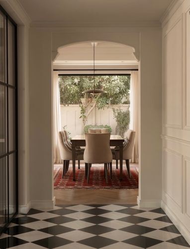 Hallway with checkerboard floor leading through arched opening into dining room with garden view