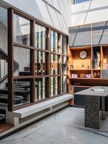 Study with terrazzo desk, timber-framed glass wall, open shelving, and mosaic staircase beyond