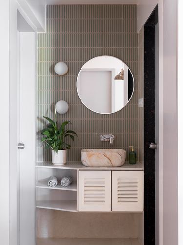 Bathroom vanity with round mirror, marble vessel sink, and fluted green tile wall