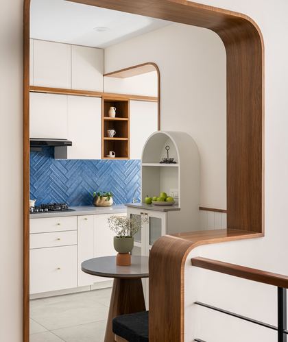 View through curved wooden archway into white kitchen with blue herringbone tile backsplash