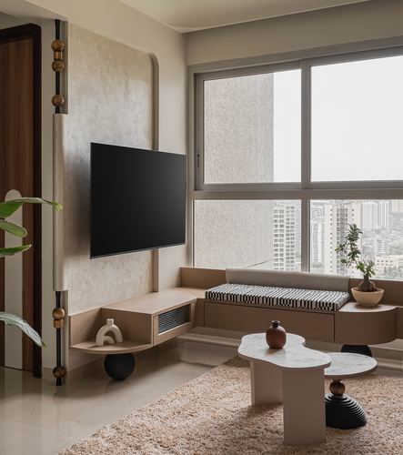 Living room corner with curved plaster wall, wall-mounted TV, window seat and sculptural coffee tables