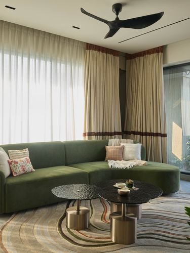 Curved olive green sofa with round textured coffee tables in a sunlit corner living room