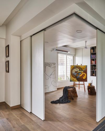 White sliding doors open to a small art studio with an easel, wood floor, and bookshelf