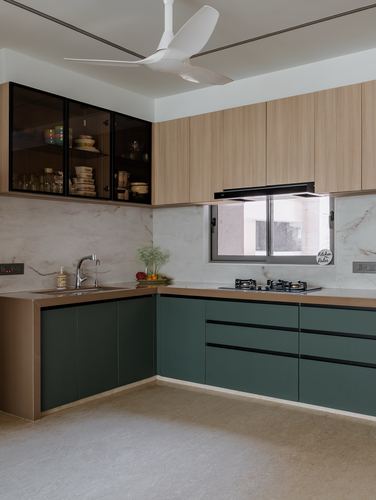 L-shaped kitchen with green base cabinets, light wood uppers, and marble-look backsplash