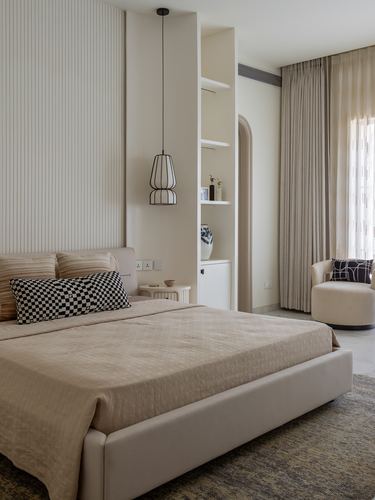 Beige minimalist bedroom with fluted wall panel, arched doorway, and cage pendant light over bed