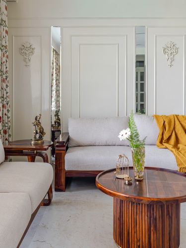 Living room with wood sofas, fluted round coffee table, and paneled mirrored wall
