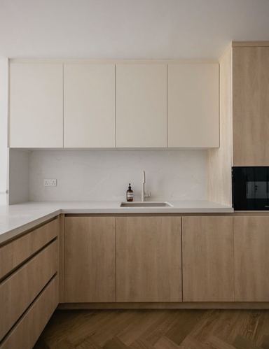 Minimalist kitchen with light wood lower cabinets, white upper cabinets, and stone counter with sink