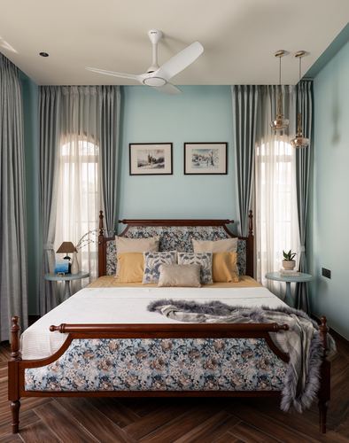 Powder blue bedroom with carved wooden four-poster bed and arched curtained windows