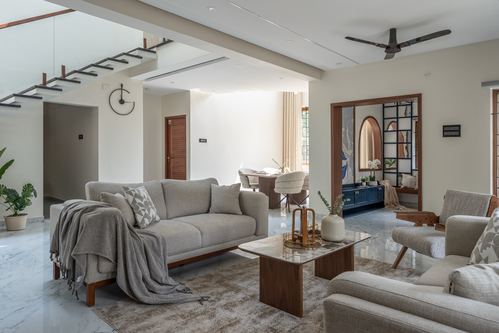 Open-plan living room with grey sofas, marble floor, floating staircase, and framed view into a blue console area beyond.