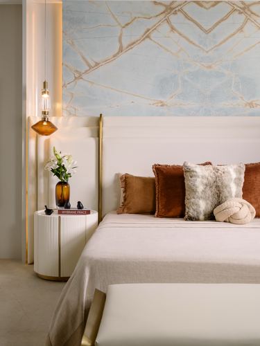 Bedroom with tufted headboard, rust and faux-fur cushions, fluted nightstand and marbled mural wall