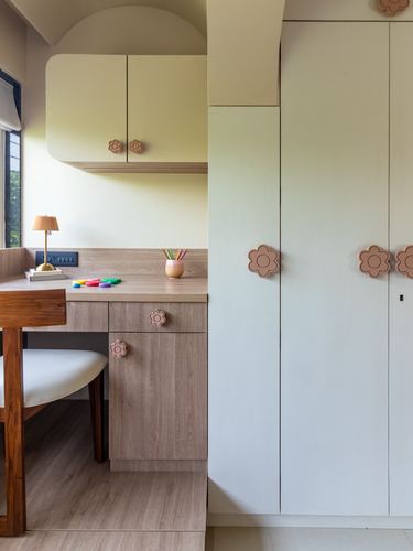 Child's study nook with pale yellow cabinetry and wooden desk featuring flower-shaped drawer pulls