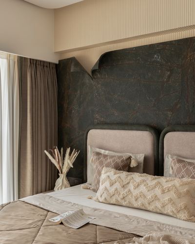 Bedroom with dark textured stone wall, upholstered headboards, and beige bedding with dried pampas grass accent.