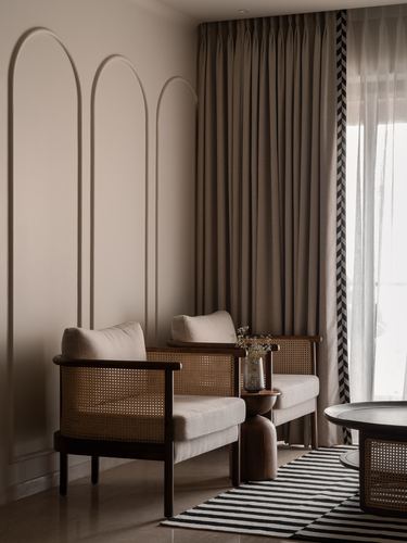 Two cane armchairs beside arched wall mouldings and pleated curtains in a warm-toned living room