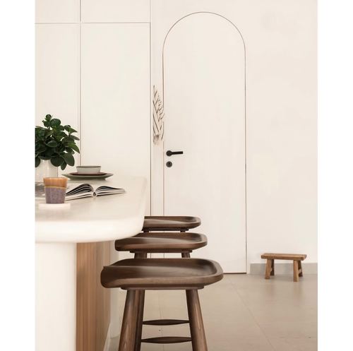 Rounded stone kitchen island with walnut stools beside an arched white door
