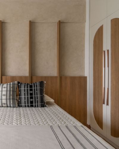 Bedroom corner with wood-panelled headboard wall and arched wardrobe with brass handles