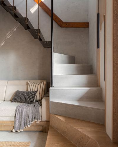 Cream sofa beneath a suspended metal staircase beside a solid concrete stair in a minimalist home