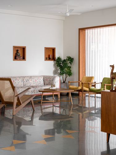 Living room with cane armchair, floral sofa, terrazzo floor and wall niches holding a buddha statue
