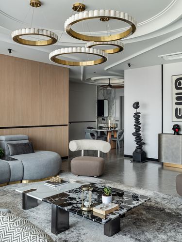 Living room with tiered brass ring chandelier, marble coffee table and black sculptural totem