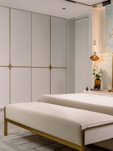 Bedroom with gold-lined wardrobe, cream bench, and pendant light beside bed with lilies