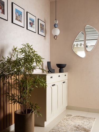 Foyer with pink plaster wall, gallery frames, cream cabinet, plant, and an organic mirror