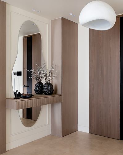 Foyer with oval mirror over ribbed wood console, black vases, and a dome pendant light