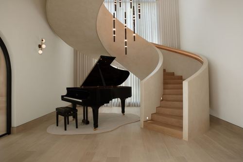 Black grand piano beneath a curved plaster staircase with hanging pendant lights, Dubai villa