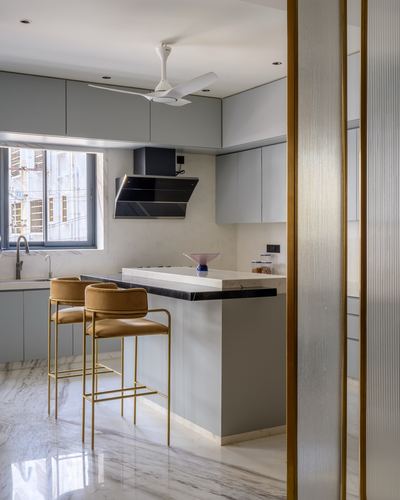 Modern grey kitchen with marble backsplash, black island counter, mustard bar stools, and brass door frame.