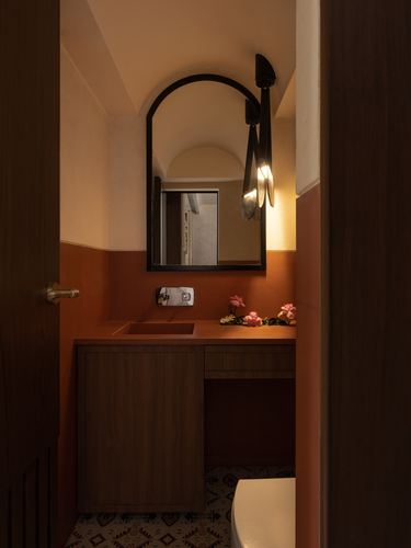 Terracotta powder room seen through a doorway with arched mirror and warm sconce light