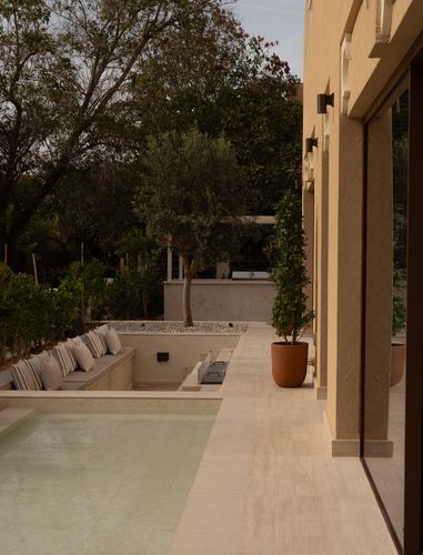 Villa terrace with pool, sunken bench seating, olive tree, and stone-clad walls in golden light
