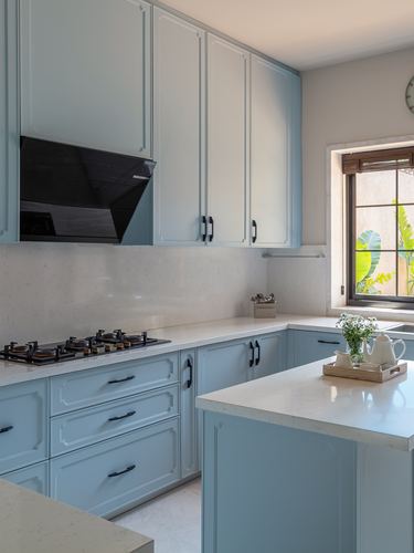 Powder blue kitchen with white countertops, black chimney hood, and island under a garden-view window