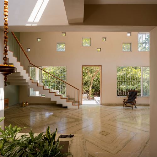 Double-height foyer with stone floor, floating staircase, punched square windows and garden view beyond