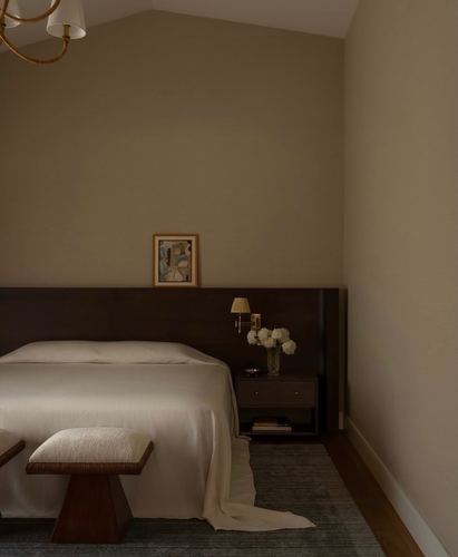 Bedroom corner with dark wood headboard, brass sconce, nightstand and boucle bench under a sloped ceiling