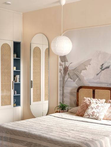 Bedroom with cane wardrobe, oval cane-framed mirror, paper pendant light and mural headboard wall