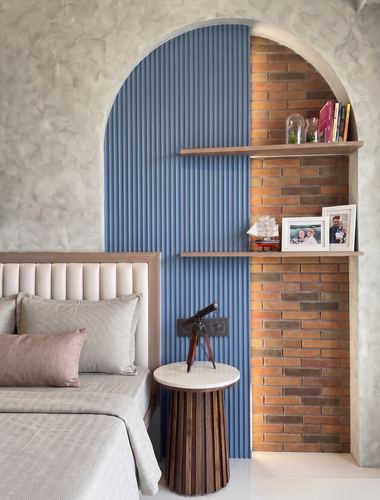 Arched wall niche with blue fluted panel and exposed brick shelves beside a padded bed headboard