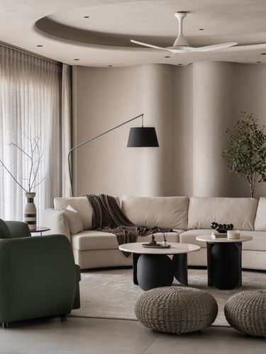 Curved beige living room with cream sofa, black side tables, and green armchair under arc lamp