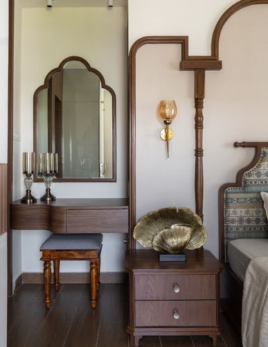 Wooden dressing table with arched mirror beside a carved bed panel and brass wall sconce