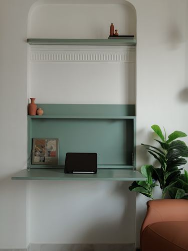 Sage green fold-down desk in arched wall niche with terracotta vases and a fiddle leaf fig plant beside it