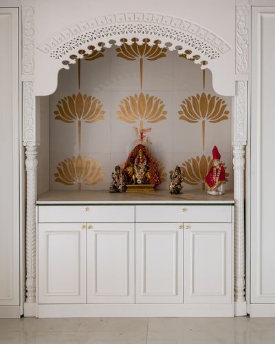 White carved pooja unit with gold lotus tile backdrop and deity idols on marble counter