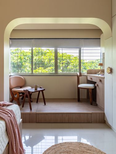 Arched alcove with a raised wooden platform, pink chair, and window overlooking green trees.
