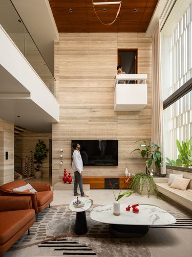 Double-height living room with stone-clad wall, cantilevered white balcony, and two men looking up