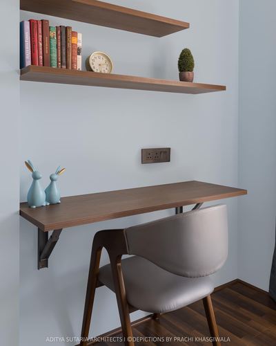 Wall-mounted wooden desk with grey chair under floating bookshelf against pale blue wall