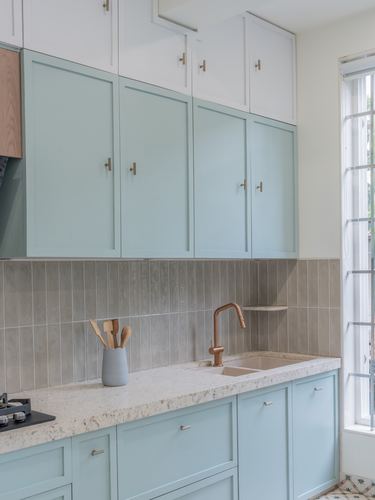 Pastel blue and white kitchen cabinetry with granite countertop and brass faucet