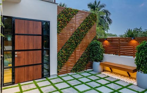 Terrace entry with wooden door, slatted wood wall with diagonal vertical garden, and checkerboard grass flooring
