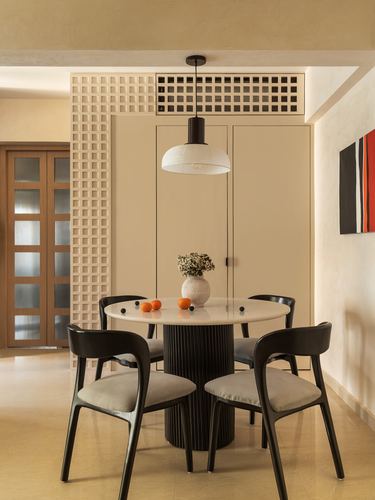 Round stone-top dining table with black chairs under a dome pendant, framed by a lattice screen