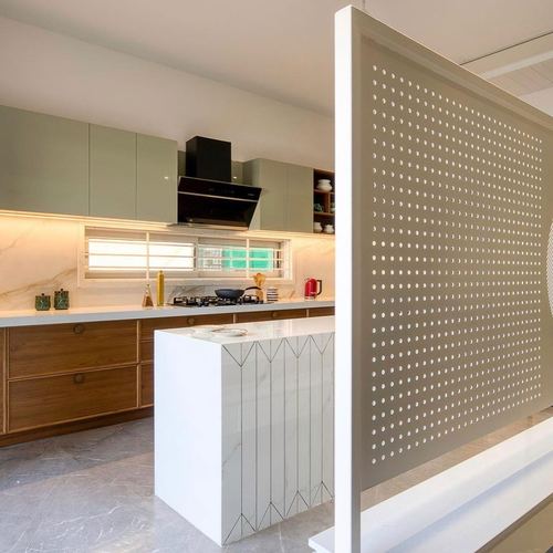Sage green and wood kitchen with marble-look island beside a perforated metal divider panel