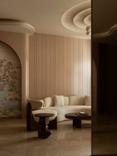 Curved cream sofa in warm beige living room with arched mural niche and sculptural wood table